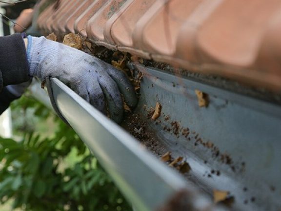 Bladeren uit verstopte dakgoot halen