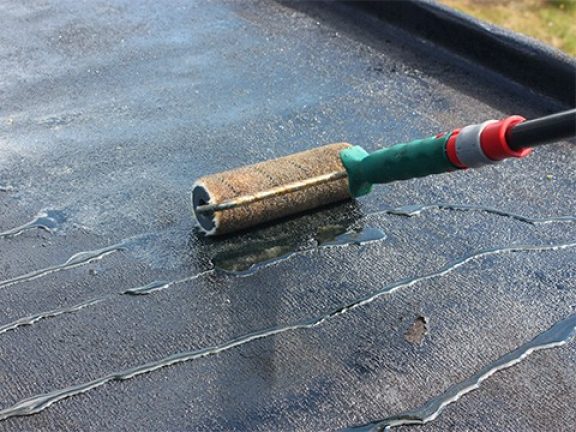 Lijm wordt uitgesmeerd op het dak met een roller